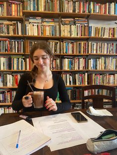 a woman sitting at a table in front of a book shelf filled with books and papers