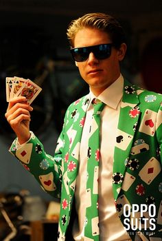 a man in a green suit and sunglasses holding up playing cards while wearing shades on his face