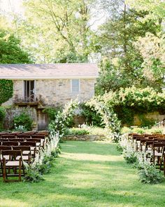 an outdoor ceremony set up with wooden chairs and flowers on the grass in front of a stone building