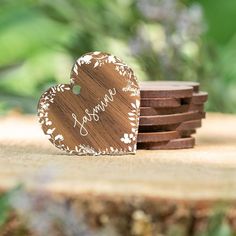 a heart shaped wooden sign sitting on top of a pile of wood coasters next to some purple flowers