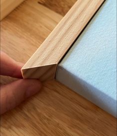 a hand is holding the edge of a piece of wood on top of a wooden floor