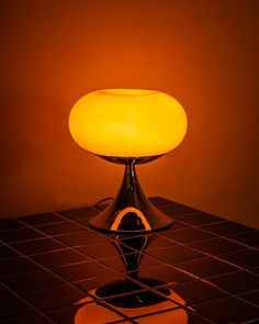 an illuminated table lamp sitting on top of a tiled floor in front of a wall