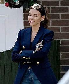 a woman in a blue blazer and jeans is smiling at the camera with her arms crossed