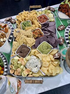 a table filled with different types of snacks and dips on trays next to plates