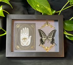 two hand prints in a shadow box on a black background with green leaves and gold accents