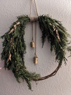 a wreath hanging on the wall with two bells attached to it and evergreen leaves around it