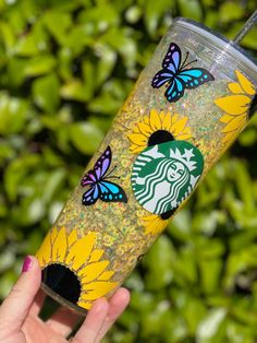 a starbucks cup with sunflowers and butterflies on it is being held up by a hand