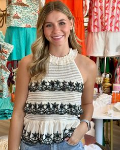 a woman standing in front of a rack of clothing and smiling at the camera with her hands on her hips