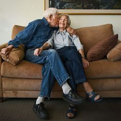 an older man and woman sitting on a couch in front of a large art piece