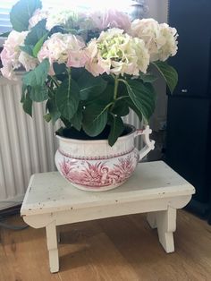 a white and pink flower pot sitting on top of a wooden table next to a radiator