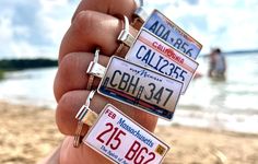 a person holding three license plates in front of the ocean and people swimming in the water