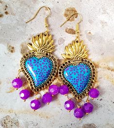 Beautiful and unique handmade earrings delicately brush painted with Talavera style flowers in purple and aqua green and adorned with glass beads, protected with several layers of jewelry varnish, to protect the paint and look even more beautiful. These sacred heart earrings are inspired by Frida Khalo and hand painted Talavera style, part of our Mexican culture, they are the ideal complement for any occasion that will surely enhance your beauty since they are unique pieces, the ideal gift for Mother's Day and holidays. Features/ Product info The Main Material: Zinc Alloy (Golsd) Color: Aqua and purple - Earrings: 3 in (H) 1.75 (W) -Earrings weight: 8 grams (each) -The hooks are stainless steel and 14k gold plated. Jewelry Love: Your Essential Guide to Caring for Your Treasures -Avoid tang Handmade Bohemian Dangle Heart Earrings, Hand Painted Drop Earrings For Festivals, Bohemian Dangle Heart Earrings, Bohemian Hand Painted Earrings For Festivals, Bohemian Hand Painted Heart Earrings As Gift, Bohemian Earrings For Valentine's Day, Bohemian Style Pierced Heart Earrings, Bohemian Hand Painted Purple Earrings, Purple Hand Painted Bohemian Earrings