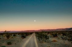 a dirt road in the middle of an open field with mountains in the background at dusk