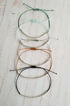 four bracelets with pearls on them sitting on a white wooden floor