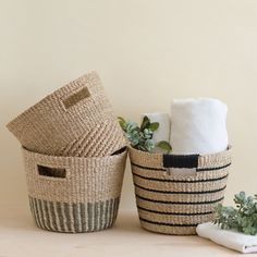 two woven baskets with towels and plants in them on a wooden table next to a towel holder