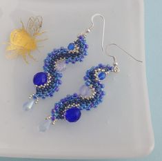 These stunning ocean wave statement drop earrings are hand stitched from tiny glass beads and larger faceted glass beads in shades of blue, and silver with a hint of purple. They curve beautifully into the wave shape and are finished with pale iridescent blue glass drops. They were inspired by the sea. The earrings are approx 6cm long, not including the earwires, so perfect if you love longer earrings. The earwires are Sterling silver.  They will be sent in a small gift box and would make a love Blue Drop Earrings With Bead Caps, Blue Beaded Drop Earrings With Bead Caps, Blue Bead Cap Drop Earrings, Elegant Blue Beaded Earrings, Iridescent Blue, Sea Inspired, Statement Drop Earrings, Bead Work Jewelry, Small Gift Boxes