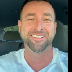 a man smiling in the back seat of a car with his eyes wide open and wearing a white shirt