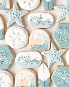 baby shower cookies are arranged on a white tablecloth with blue and pink decorations, including starfish, seashells, stars