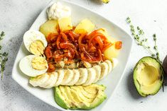 a white plate topped with sliced up bananas and other foods next to an avocado