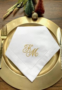 the monogrammed napkin is sitting on top of a gold plate with silverware