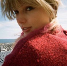 a close up of a person wearing a red sweater near the ocean with a cell phone in her hand