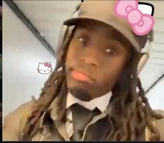 a man with dreadlocks wearing a hello kitty hat and bow tie is looking at the camera