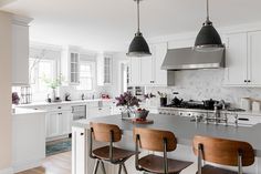 a kitchen with white cabinets and wooden stools in front of an island countertop