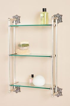 three glass shelves on the wall with soap, shampoos and other bathroom items