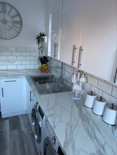 a white kitchen with marble counter tops and appliances in front of a clock on the wall