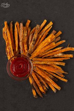 french fries with ketchup on a black surface next to a small glass bowl