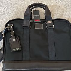 Tumi Unisex Slim Briefcase. Black Ballistic Nylon With Brown Trim. 16” X 12” X 2”. Has Multiple Pockets Inside And Out And Removable/Adjustable Shoulder Strap. Zipped Bottom To Slide On To Rolling Suitcase Handle. Never Used, Pristine Condition. Modern Black Briefcase With Leather Trim, Designer Black Luggage With Sleeve, Business Briefcase With Leather Trim In Black, Black Leather-trimmed Briefcase For Business, Black Leather Trim Briefcase For Business, Designer Black Laptop Bag For Business, Nylon Briefcase With Luggage Sleeve For Business, Business Briefcase With Luggage Sleeve In Nylon, Luxury Black Luggage With Adjustable Strap