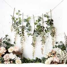 flowers and greenery are hanging from a string on a wall in front of a white background