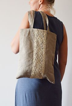 a woman carrying a large bag with lace on the front and sides, standing against a white wall