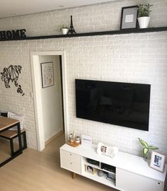 a flat screen tv mounted on a white brick wall in a living room next to a dining table