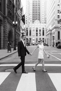 a man and woman walking across a crosswalk in the middle of a city holding hands