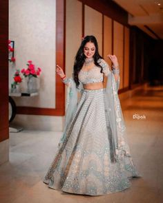 a woman in a white and blue lehenga with her hands out to the side