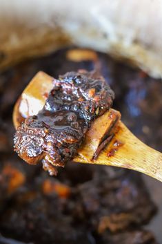 a wooden spoon full of cooked meat and sauce in a crock pot with some bread on the side