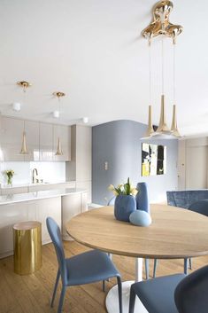 a dining room table with blue chairs and gold accents on the walls in an open concept kitchen