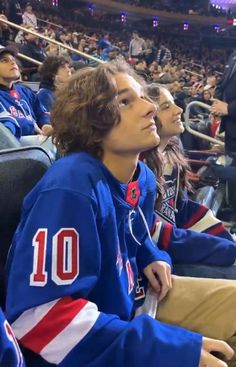 a young man sitting in the stands at a hockey game wearing a blue jersey with red and white stripes