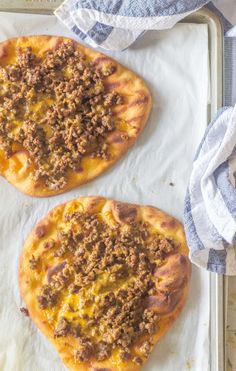 two homemade pizzas sitting on top of a baking sheet covered in cheese and meat