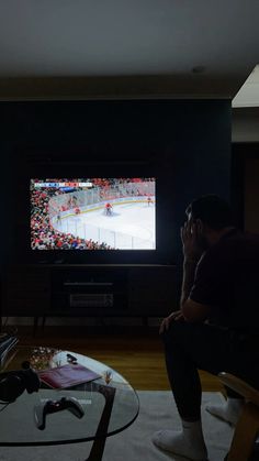 a man sitting in front of a tv watching a hockey game on the big screen