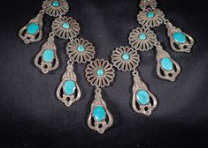 This is an unusual and beautiful vintage statement necklace. Quite bohemian in style are seven daisy flower heads, each having a turquoise blue enamel centre, from each flower hangs an art nouveau style pendant each with turquoise blue enamel cabachons, the centere one is slightly larger than the other six. The decorative elements of this necklace are attached to its chain by two decorative hangers. Visually striking and quite heavy, with the addition of more chain would look great as a low slun Vintage Blue Flower Pendant Necklace, Vintage Turquoise Filigree Necklace, Vintage Blue Turquoise Metal Necklace, Vintage Blue Flower Pendant Jewelry, Bohemian Blue Flower Pendant Jewelry, Vintage Turquoise Necklace In Metal, Decorative Hangers, Art Nouveau Style, Decorative Elements