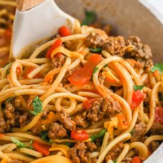 a close up of a plate of spaghetti with meat and vegetables on it, with a wooden spoon in the bowl