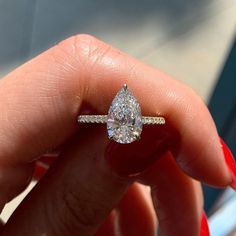 a woman's hand holding a ring with a pear shaped diamond on top of it