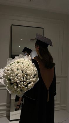 a woman holding a bouquet of white roses in front of a mirror with a graduation cap on her head