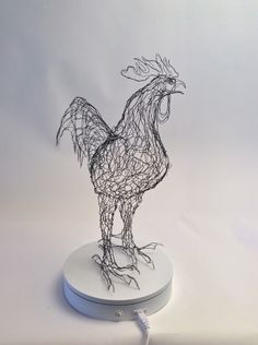 a wire sculpture of a rooster on a white surface with a charger plugged into it