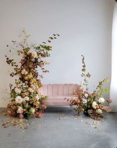 a pink couch sitting next to flowers and greenery on top of a gray floor