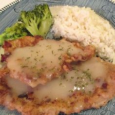 a blue plate topped with meat covered in gravy next to rice and broccoli