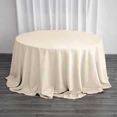 a round table with a white cloth draped over it on top of a hard wood floor