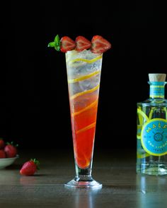 a tall glass filled with liquid and strawberries next to a bottle of alcohol on a table